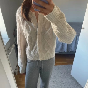 Beige stickad kofta från Cubus - Supermysig beige stickad kofta från Cubus i storlek XS. Koftan har ett snyggt kabelstickat mönster framtill, ribbade muddar och knappar hela vägen. Perfekt att slänga på sig över en t-shirt eller linne när det är kyligt ute.