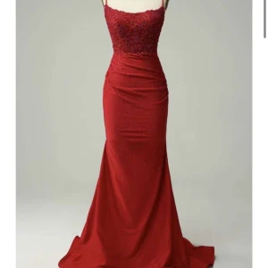 Röd långklänning med spets och öppen rygg - Säljer en röd långklänning med smala axelband och öppen rygg. Klänningen har glittriga detaljer, spets upptill och figurnära passform. Perfekt för bal eller fest, med snygg slits och v-ringning framtill.  Använd 1 gång och ser ut som ny! 