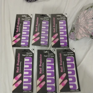 Lila nagelskydd tejp för nail art - Säljer flera förpackningar med lila peel off tape för nagelskydd vid nail art. Varje paket innehåller 10 stycken skydd i böjd form som enkelt fästs runt nageln för att undvika kladd vid lackning. Perfekt för dig som gillar att fixa naglarna hemma och vill ha skarpa kanter.