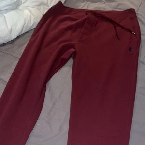 Vinröda mjukisbyxor Polo Ralph Lauren - Snygga vinröda mjukisbyxor från Polo Ralph Lauren med dragsko i midjan och ribbade muddar vid bensluten. Byxorna har en liten blå logga broderad på ena benet och är gjorda i mjuk bomullsmix. Perfekta för chill eller träning.