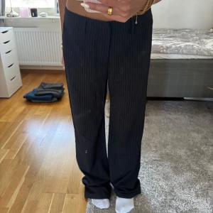 Svarta randiga kostymbyxor Madlady - Snygga svarta kostymbyxor från Madlady med tunna vita ränder. Byxorna har raka, lite loose ben och klassisk passform med hällor för bälte. Perfekta för en clean och trendig look. Materialet känns mjukt och följsamt.  Säljer pga för stora, aldrig använda. Helt nya.