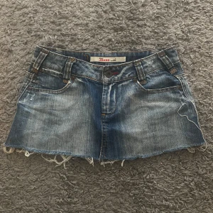 Blå jeanskjol från Only med fransig kant - Snygg blå jeanskjol från Only med slitna detaljer och fransig rå kant. Klassisk femficksmodell med bälteshällor och knappstängning. Perfekt för dig som gillar en avslappnad och trendig stil.