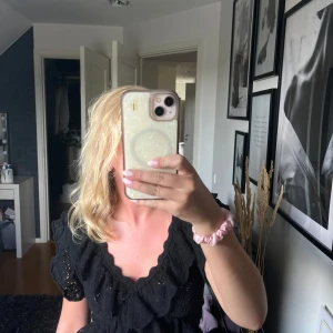 Svart volangblus med spetsdetaljer - Supersöt svart blus med djup v-ringning, volanger och spetsdetaljer. Toppen har korta ärmar och är croppad med ribbad nederkant. Perfekt för dig som gillar romantisk och trendig stil.