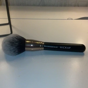 Hickap Powder Deluxe sminkborste - Stor och fluffig sminkborste från Hickap, modell 111 Powder Deluxe. Borsten har svart handtag, metallfärgad hylsa och täta, mjuka syntetstrån i svart och vitt. Perfekt för att applicera puder eller bronzer med en jämn finish.