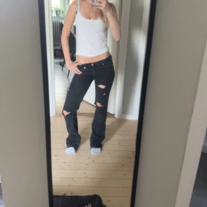 Svarta slitna bootcut jeans - Säljer ett par svarta jeans med bootcut-modell och slitna detaljer över knäna. Byxorna är från början högmidjade men har sytt om och sedan gjort hålen själv