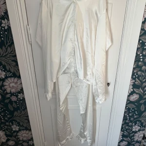 Vit satinpyjamas från LMTD, strl 158/164 - Snygg vit pyjamas från LMTD i glansigt satinmaterial. Setet består av en långärmad skjorta med knappar och matchande byxor. Byxorna är i samma material som skorpan, med en lätt volang längst ner på byxan! Skjortan har klassisk krage och ärmar med lätt volang vid ärmslut. Perfekt för dig som gillar en skön och mysig pyjamas! Lappen är kvar, aldrig Andvänd