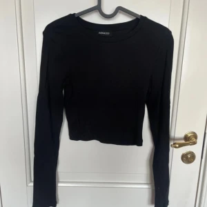 Svart ribbad långärmad topp Even&Odd - En svart, croppad långärmad topp från Even&Odd. Toppen är ribbad och har en rund halsringning. Perfekt att styla med höga jeans eller kjol för en clean look.