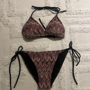 Design by Si bikini - Snygg bikini med svart och rosa mönster, trekants-bh med knyt i nacken och ryggen samt matchande trosa med knyt i sidorna. Aldrig använd
