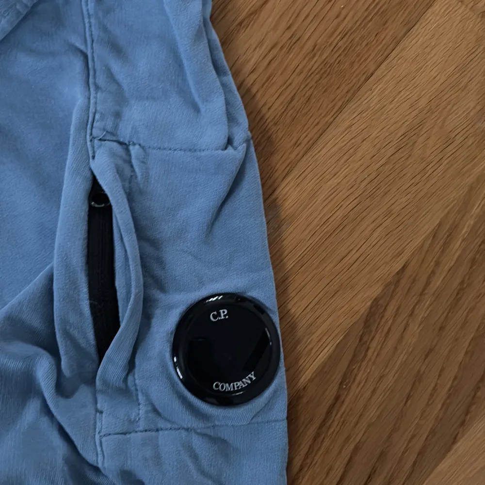 Säljer en snygg blå sweatshirt från C.P. Company. Tröjan har långa ärmar och en rund halsringning. På ärmen finns en cool detalj med en ficka och en rund logotyp. Perfekt för en avslappnad stil. Pris går att diskuteras.. Neuletakit & Villapaidat.
