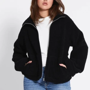Svart teddyjacka med dragkedja - Mysig svart teddyjacka med dragkedja framtill. Perfekt för kyliga dagar med sin fluffiga och varma design. Jackan har en avslappnad passform och två fickor framtill. Använd 1 gång!