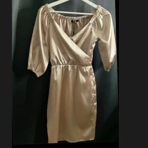 Champagnefärgad omlottklänning från Bik Bok - Snygg champagnefärgad klänning från Bik Bok i omlottmodell. Klänningen har trekvartsärmar och en elastisk offshoulder-design som ger en chic look. Perfekt för att sticka ut med stil!(helt ny med pris lapp)