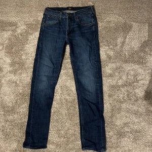 Mörkblå jeans från Lee - Säljer ett par mörkblå jeans från Lee med klassisk femficksdesign och dragkedja. De har en slim passform och är perfekta för en avslappnad stil. Lite slitningar på både fram och baksida.