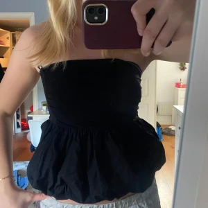 Svart tubtopp från Gina Tricot - Säljer en snygg svart tubtopp från Gina Tricot. Toppen har en volangdetalj nedtill som ger en fin siluett. Perfekt för att styla med olika outfits. Hör av dig vid intresse!