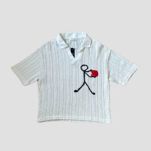 Heartgiver V-Neck / Piketröja - En vit stickad pikétröja med ett unikt broderi av en figur som håller en röd hjärta. Tröjan har korta ärmar och en klassisk krage. Perfekt för en avslappnad stil.