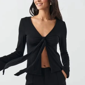 Svart långärmad topp med knyt - Snygg svart långärmad topp med knyt framtill. Perfekt för en stilren look med en twist. Toppen har en djup v-ringning och är tillverkad i ett mjukt material. Använd 2 gånger där av som ny!!