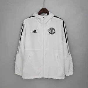 Vit vindjacka från Adidas - Säljer en stilren vit vindjacka från Adidas med Manchester United-logga på bröstet. Jackan har svarta ränder längs ärmarna och en praktisk dragkedja framtill. Perfekt för fotbollsfans! 🏆