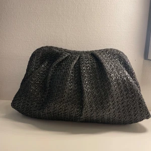Svart clutch - Snygg svart clutch med en unik textur. Väskan har en rymlig öppning och är perfekt för att bära med sig det nödvändigaste. Den har en stilren design som passar till många olika tillfällen.
