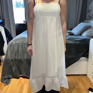 Vit långklänning med knyt - Säljer en vit långklänning med smala axelband och en söt knytning i ryggen. Klänningen har en volangdetalj längst ner, Den är luftig och bekväm att bära.