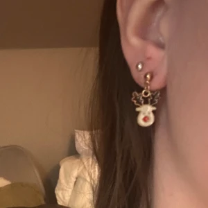 Söta renörhängen med röda detaljer - Charmiga örhängen i form av renar med små röda detaljer. Perfekta för att ge en lekfull touch till din outfit. De har en guldig bas och är lätta att bära.