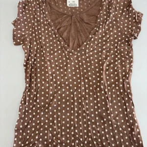 Brun prickig v-ringad topp - Säljer en brun topp med vita prickar och v-ringning. Toppen har korta ärmar och är perfekt för en avslappnad stil. Passar bra till jeans eller kjol.
