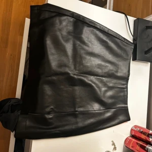 Svart skinnkjol - Snygg svart skinnkjol i kort modell. Perfekt för en trendig look. Kjolen har en tight passform och är tillverkad i ett stilrent material som ger en cool känsla.