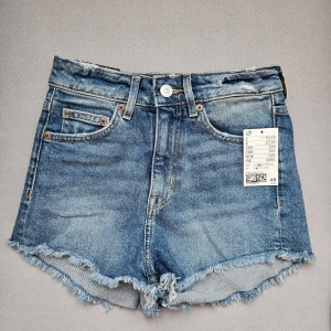 Blå jeansshorts från H&M - Snygga blå jeansshorts från H&M med hög midja och fransiga kanter. Perfekta för sommarn!