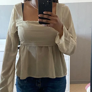 Beige blus från BikBok - Säljer en stilren beige blus från BikBok med långa ärmar och fyrkantig halsringning. Blusen har en lätt och luftig passform som ger en elegant look. Perfekt för att klä upp eller ner beroende på tillfälle.