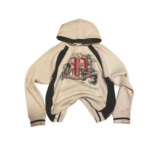 Skater hoodie med tryck - Säljer en vit skater hoodie med svart och rött tryck framtill. Den har svarta detaljer längs sidorna och ärmarna. Perfekt för en avslappnad stil då den är baggy/ oversized!! 