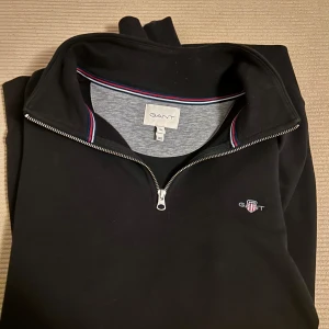 Svart half zip från GANT - Säljer en helt ny half zip från GANT i storlek XL som endast är testad. Säljer pga den är för stor.