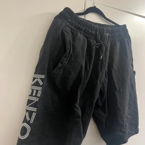 Svarta shorts från Kenzo - Snygga svarta shorts från Kenzo med elastisk midja och dragsko. Shortsen har två sidofickor och en stor Kenzo-logga längs benet. Perfekta för en avslappnad stil.