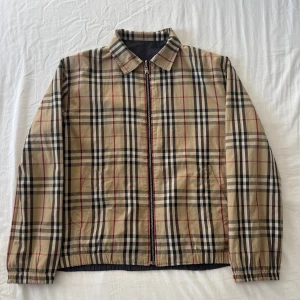 Burberry Jacka - Vintage Burberry jacka som är reversibel.  Ingen storleks etikett men passar Medium.  Burberry monogrammet är i fint skick men det finns ett litet hål som har blivit ihopsytt. Men det syns verkligen inte. (bild 3 ovanför fickan) Den svarta sidan har blivit mer skadad och har blivit ihopsytt. Syns bara på nära avstånd.