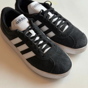 Svarta Adidas sneakers med vita detaljer - Snygga svarta Adidas sneakers med klassiska vita ränder och snörning. Storlek 40, mycket fint skick! Perfekta för en avslappnad stil. 