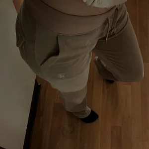 Beiga Juicy Couture - Snygga beige mjukisbyxor med snörning i midjan. Byxorna har en avslappnad passform och praktiska fickor både fram och bak. Perfekta för en bekväm och stilren look.