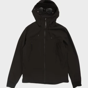 Svart vindjacka med huva och glasögon - Säljer en cool svart vindjacka med inbyggda glasögon i huvan. Jackan har dragkedja framtill och två fickor med dragkedja. Perfekt för blåsiga dagar och ger en unik look.( Cp company)