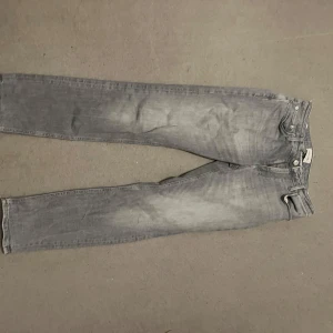 Grå jeans från Jack & Jones - Snygga grå jeans från Jack & Jones med en klassisk design. De har en dragkedja och knapp framtill samt två bakfickor. Perfekta för en avslappnad stil. W30 L32