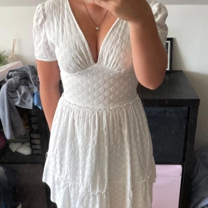 Vit kortklänning med broderade blommor - Supersöt vit kortklänning från Sinsay i storlek XXS. Klänningen har djup v-ringning, korta puffärmar och broderade små blommor över hela tyget. Den har markerad midja och volangig kjol som ger en romantisk vibe.