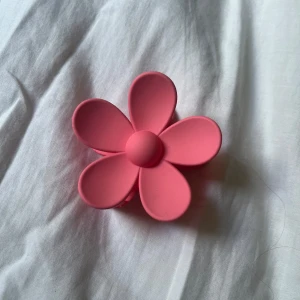 Rosa blomformad hårklämma - Supergullig hårklämma i form av en blomma helt i matt rosa plast. Klämman är rejäl och håller håret på plats. 