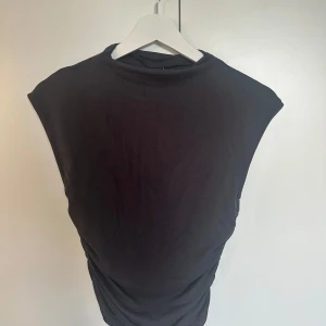 Grå ärmlös topp från Gina Tricot - En grå, enkel och stilren ärmlös topp från Gina Tricot. Toppen har en rund halsringning och är gjord i mjuk bomull, perfekt att matcha med jeans eller kjol för en clean look.