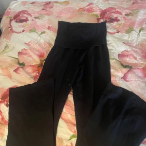 Svarta vida byxor låg midjad  - Svarta byxor med låg midjade byxor och vida ben. Mjukt material som känns skönt mot huden och ger en avslappnad look. Perfekta för dig som gillar bekväma och stilrena plagg med lite extra edge. Det är vit  tråd på byxorna.