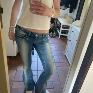 Lågmidjade bootcut jeans Gina Tricot - Snygga lågmidjade jeans från Gina Tricot i ljusblå tvätt med bootcut-ben. Jeansen har klassiska fickor fram och bak, samt slitna detaljer för en cool look. Perfekta för dig som gillar 00-talsvibbar och vill ha ett par jeans med lite extra attityd.