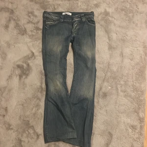 Blå jeans från Stradivarius - Säljer ett par blå jeans från Stradivarius med snyggt slitna detaljer och kontrastsömmar. Jeansen har klassisk femficksdesign, raka ben och coola broderier på bakfickorna. Perfekta för en avslappnad och trendig look.