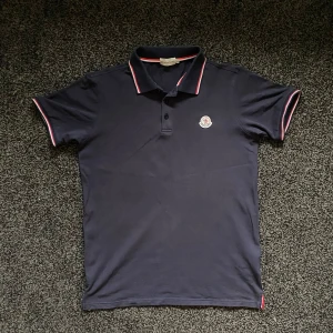 Mörkblå Moncler piké  - Snygg mörkblå pikétröja från Moncler i storlek L. Relativt liten i storleken så skulle säga att den även passar M. Hör av er vid frågor