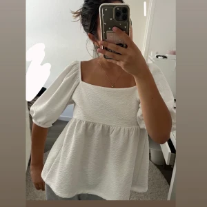 Vit blus med puffärm och snörning - Superfin vit blus med fyrkantig ringning, puffiga trekvartsärmar och snygg snörning i ryggen. Blusen har en lätt strukturerad yta och faller luftigt ned från bysten. 