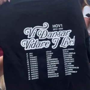SÖKER!! Svart Hov1 t-shirt Vi Dansar Vidare - Skriv om ni vet nån som säljer! Vilket pris som helst Svart hoodie  från Hov1 med stor vit text på ryggen: 'Vi Dansar Vidare I Livet' och turnédatum samt städer listade under. Klassisk passform och korta ärmar, perfekt för mig  som älskar svensk musik och vill visa ditt stöd för bandet. 