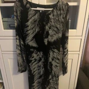 Svart och grå mönstrad klänning från Dry Lake - Snygg långärmad klänning från Dry Lake i svart med grått mönster. Modellen har rund halsringning och ett knytband på baksidan. Storlek M💕