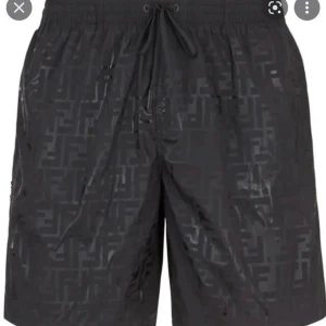 Svarta Fendi shorts med snörning - Snygga svarta shorts från Fendi med diskret mönster och elastisk midja. Shortsen har snörning i midjan och är tillverkade i ett lätt, glansigt syntetmaterial. Perfekta för sommaren och ger en clean och exklusiv vibe.