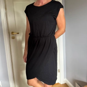 Svart mjuk klänning - Svart klänning med rund hals och resår i midjan. Klänningen har en avslappnad passform och är ärmlös, perfekt för en stilren look. Tillverkad i mjukt bomullstyg som känns skönt mot huden.