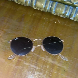 Runda ray ban solglasögon  - Snygga runda solglasögon från Ray-Ban med tunna guldfärgade metallbågar och mörka linser. Pris kan diskuteras vid snabb affär. Om du undrar över något är det bara att fråga.