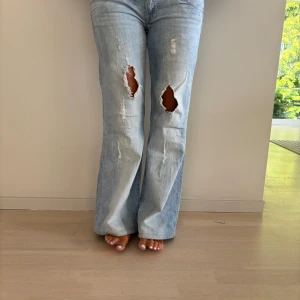 Ljusblå flare jeans från LTB - Säljer ett par ljusblå jeans från LTB med låg midja och flare-ben. Jeansen har slitna detaljer och stora hål på båda knäna för en riktigt edgy vibe. Klassisk femficksmodell i mjuk bomullsdenim. Perfekta för dig som gillar en avslappnad och trendig look.SKITSNYGGA JEANS!!. De är uppsydda. Midja: 43 innerben: 76. Jag på bilden är 162 och brukar ha storlek S/M