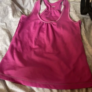 Rosa sportig linnetopp - Säljer en snygg rosa linnetopp från SOC med brottarrygg och ljusa kontrastsömmar. Toppen är gjord i ett lätt och snabbtorkande syntetmaterial, perfekt för träning. Den har en liten rynkdetalj framtill som ger en cool touch.
